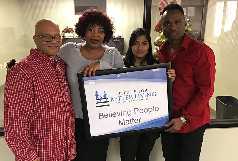 A photo of the Step Up for Better Living staff holding a sign with the organization's logo.